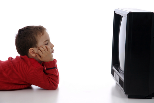 A boy laying down and watching T.V. - IN this photo a young boy is laying down and wathcing T.V.