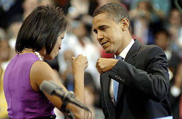 we're not telling... - Obama and Michelle Obama at podium doing fist bump, Michelle in purple dress, Obama black suit