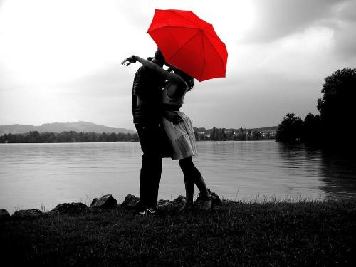 Love and Loneliness - The photo shows two lovers in their kissing scene at the bank of the river. The girl is wearing white clothes and carrying a red umbrella.