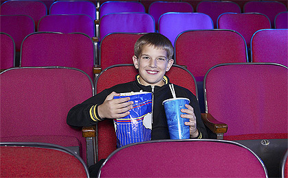 Watching A Movie - A boy in a movie theater alone and holding a large drink and popcorn.