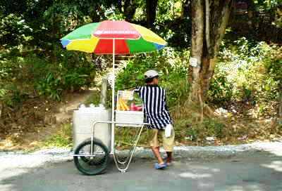 umbrella - a vendor in a cart with wheels and umbrella.