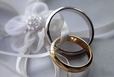 Wedding Rings - Two wedding rings [one platinum and one gold] are woven close to each other on a white satin ribbon attached to a white silk flower.