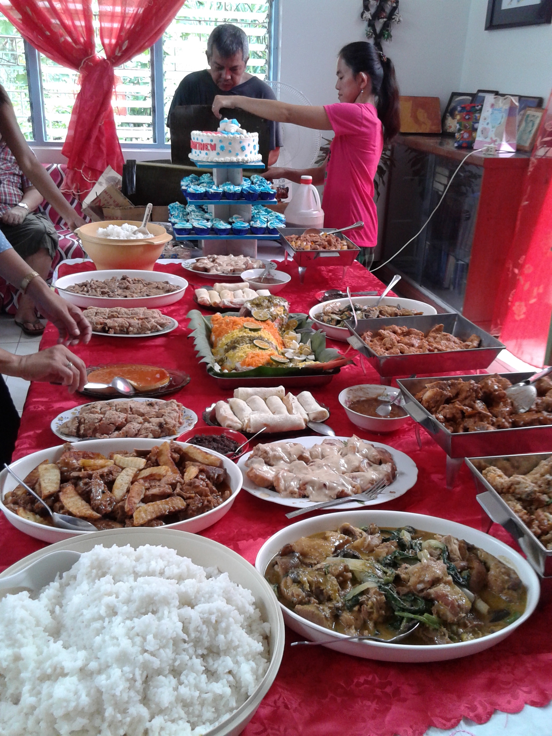 The buffet table .  The lechon is being chopped at the end table . 