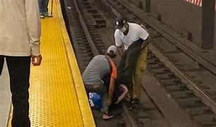 Two strangers assisting a man in a wheelchair get off of a railroad track in New York Two strangers assisting a man in a wheelchair get off of a railroad track in New York