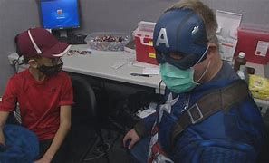 Roger Thompson dressed as Captain America giving a child an injection to his arm Roger Thompson dressed as Captain America giving a child an injection to his arm