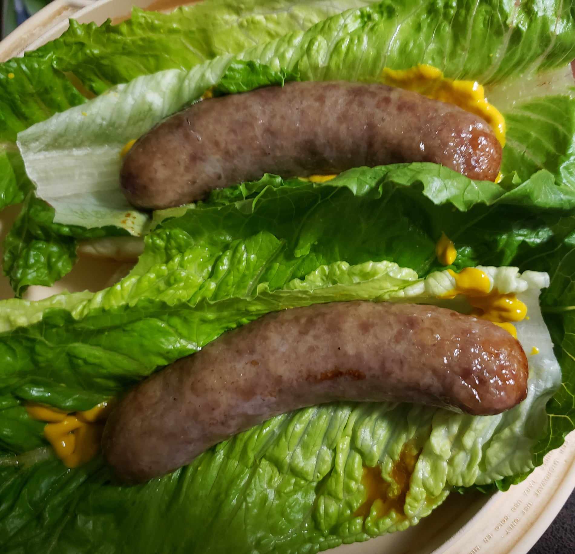 Brats wrapped in romaine lettuce with mustard on hotdog buns.