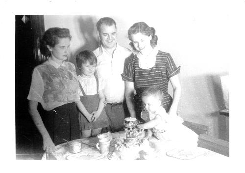 First Birthday Party December 12, 1953 - I'm adding this picture on December 2, 2006, and it will have been 53 years since it was taken come December 12.  In the picture are: Aunt Kate, Tammy (our landlord & landlady's niece), and my folks and myself.  My cake is topped with a little merry-go-round.