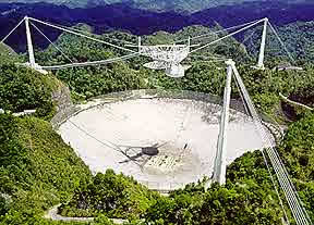 Arecibo Observatory - The Arecibo radio telescope. It search for Extraterrestrial signals from the space. The huge "dish" is 305 m (1000 feet) in diameter, 167 feet deep, and covers an area of about twenty acres. The surface is made of almost 40,000 perforated aluminum panels, each measuring about 3 feet by 6 feet, supported by a network of steel cables strung across the underlying karst sinkhole. It is a spherical (not parabolic) reflector suspended 450 feet above the reflector is the 900 ton platform