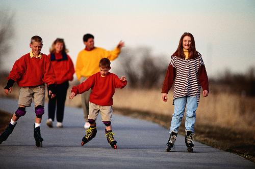 family outing - happy family bonding. Parents on walk and children playing with their roller blades.