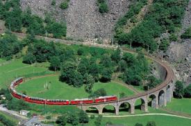 Bernina Express - Bernina Express  Bernina Express *** nominated for the UNESCO World Heritage Site.  Travel on the Bernina, the highest and steepest train crossing the alpine delight in Graubünden. There is twice as much to see as before along one of the most beautiful railway routes in the world.  The journey begins in Chur, continues along the Albula route into the Engadine and keeps on going - without cogwheels - over the Bernina Pass down to southerly Valposchiavo, over the spiralling viaduct at Brusio and on to Tirano. Cross the Alps from North to South (or vice versa) enjoying breath-taking vistas from the 1st and 2nd class panorama cars. Ride over graceful via-ducts, through switch-back tunnels, along rushing mountain streams, glaciers and even an alpine garden. Hear the narration all through the trip. The journey can also be extended to Lugano by bus in summertime. The train journey is for approximately 4hrs and the bus 3hrs.  Wagons - The wagons are the most modern, and air conditioned panoramic coaches. The only glass between you and the landscape is in your sunglasses. In the open-view coaches you can feel the sun and wind up close, hear the rushing of mountain streams and breathe fresh mountain air. Thanks to large windows extending to the top of the train, travelers are able to enjoy excellent panoramic views. Air-conditioning provides for comfortable, draft-free trips. Oh! What a feeling! It offers first and second class service as well as panoramic coaches. The variousand interesting coach options are the Stiva retica , Alpine Classic Pullman Express, The Starck Coach, Gourmino Dining Cars, Panorama Coaches, Historical Coaches and Wedding journeys. Catering There is a Minibar service available onboard the trains and on partial routes. The passengers may also purchase snacks and beverages on board.  Some useful information      * Reservations for trains and buses are compulsory and are at a surcharge     * Free «Bernina Express Certificate» for passengers available on request at Rhaetian Railway stations     * Rates include value added tax and exclude seat reservations, and are subject to change.     * A ½ price ticket allows you to travel for half price.     * The junior ticket allows children under 16 to travel free when accompanied by at least one parent.     * Railpass (GA) and day tickets are valid.     * Passport or identity card required to cross border into Tirano (Italy) for Indian passport holders valid travel documents are mandatory.