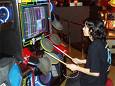 drummania arcade machine - this is a drummania arcade machine in a recreational arcade establishment. The pictue shows a person enjoying while playing drummania using his own drumsticks for easeness of hitting the drum pads.